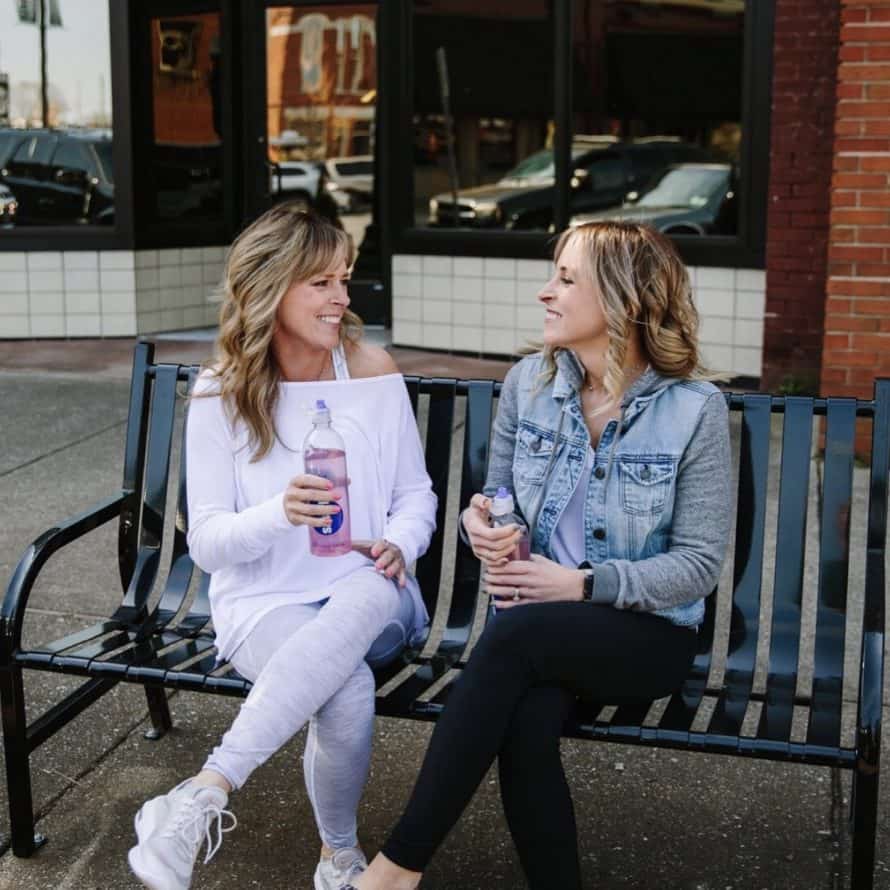 kim and kalee drinking water outside on a bench