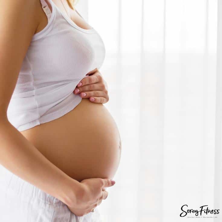woman holding her pregnant belly in a white tank top