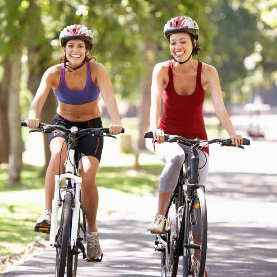2 Women on Road Bikes on a paved road with helmets on