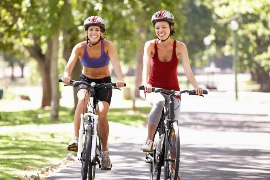 2 Women on Road Bikes on a paved road with helmets on