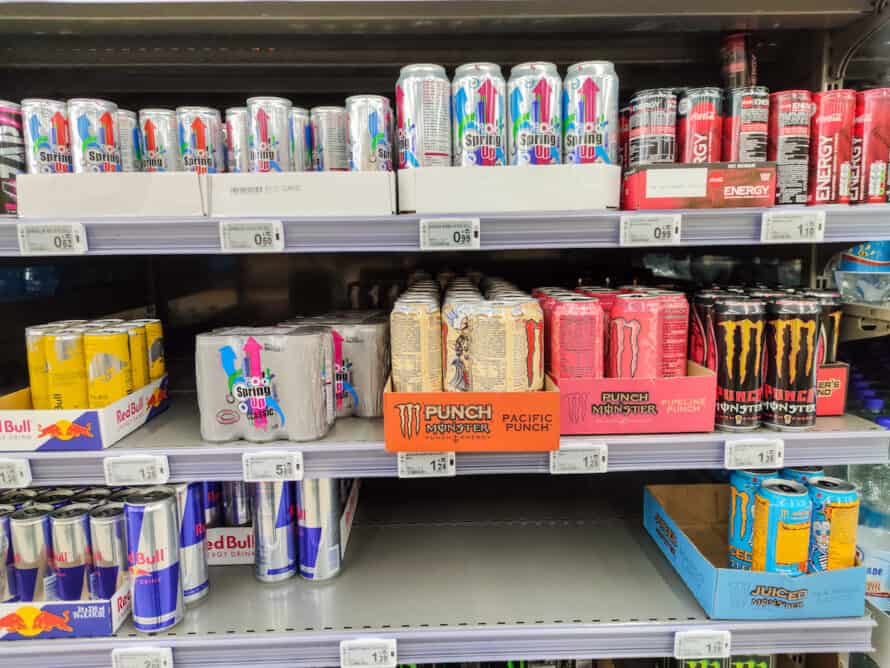 Varied range of energy drink cans with leading brands such as red bull, coca cola energy and lesser known brands punch, spring up, juiced monster display for sell in the supermarket shelves